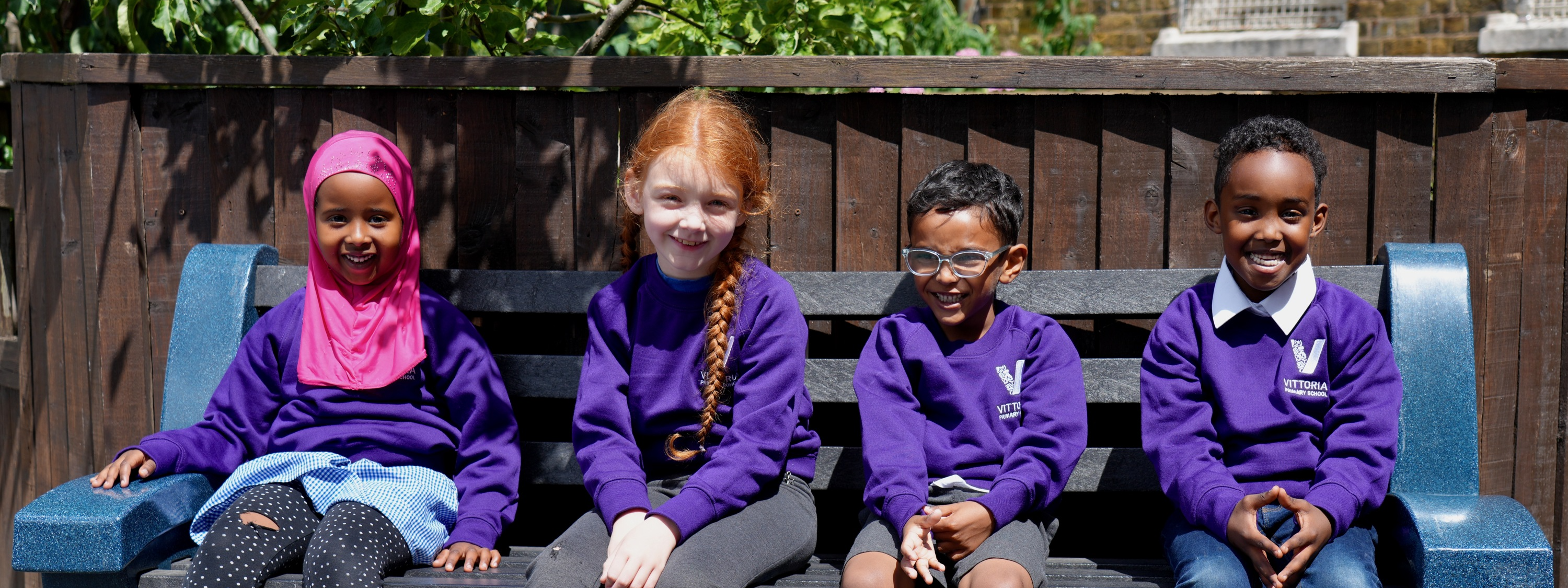 Vittoria Primary School  - Four children sitting on a bench in school uniform